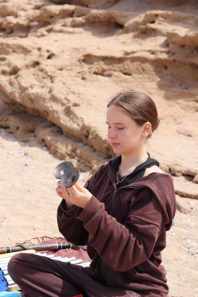 Larissa listening closely to a singing bowl on the beach.