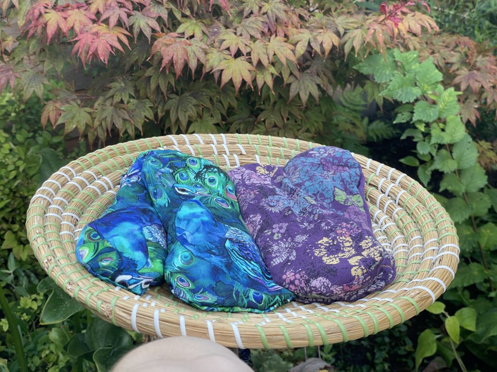 Colourful handmade eye pillows in a woven basket surrounded by greenery.